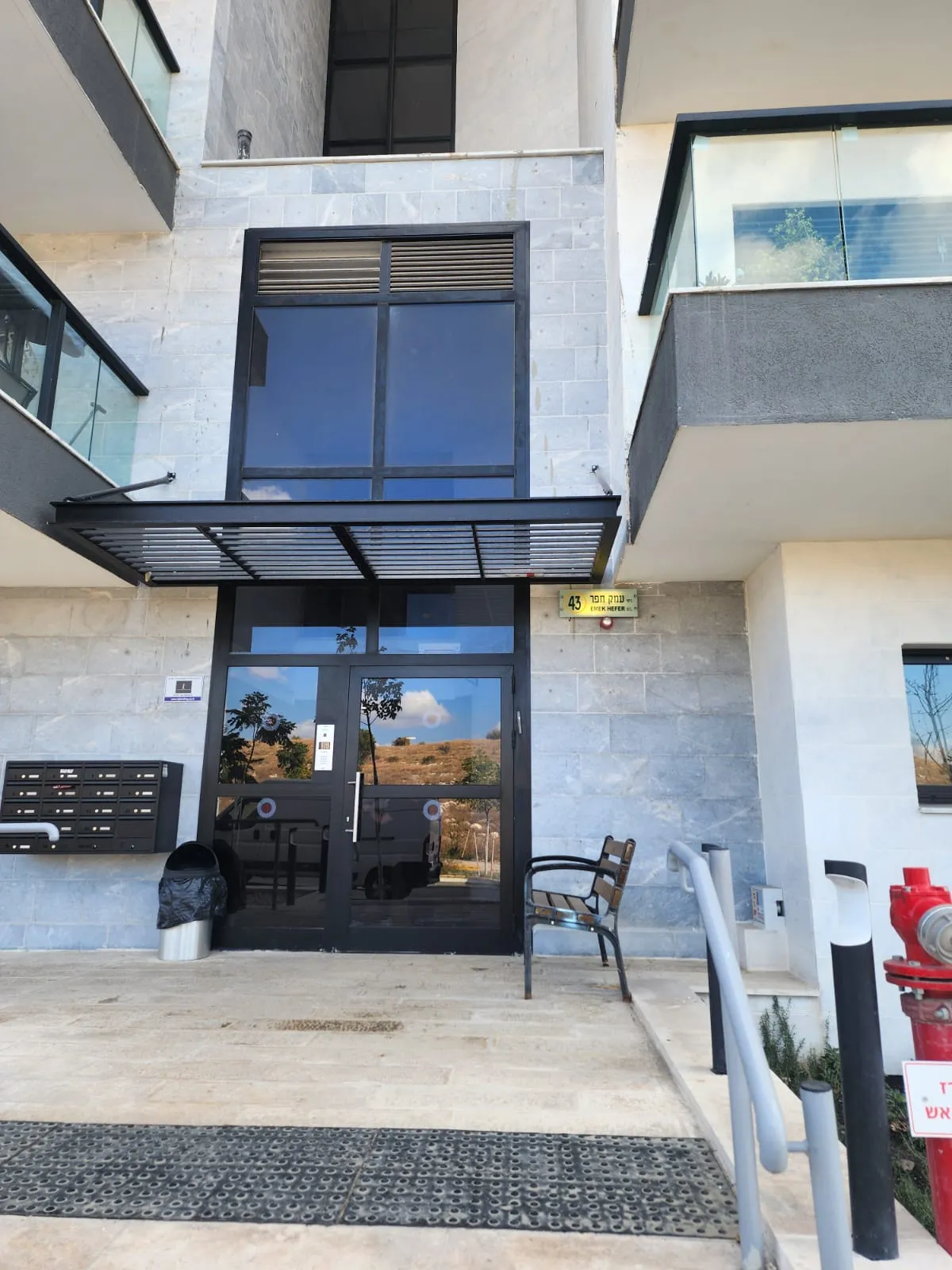 כניסה לבניין מגורים עם גגון ותיבות דואר, בניין בניהול אל ג׳י